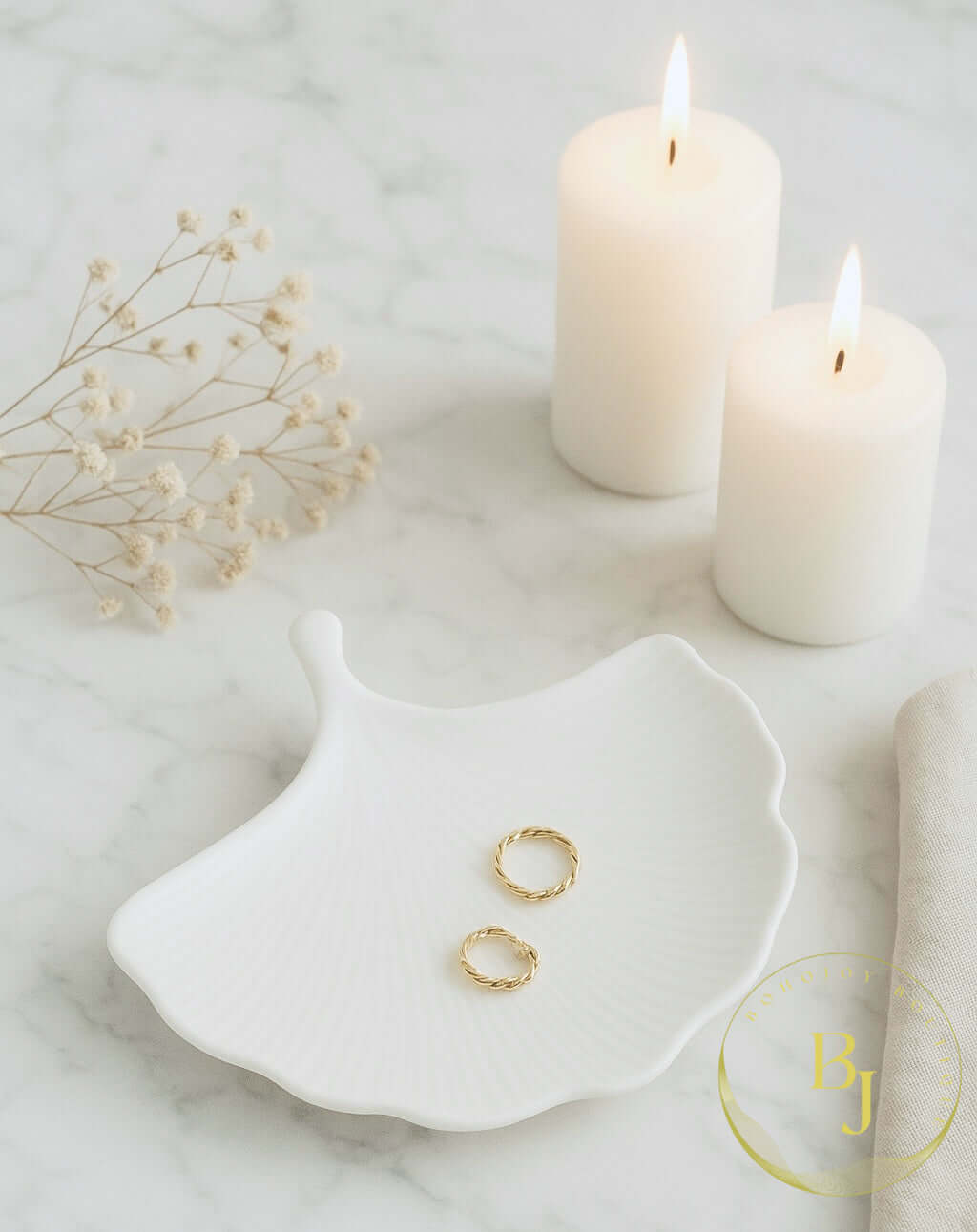 Plateau ESSENCE décoratif en blanc avec deux bagues dorées sur une table en marbre, éclairé par des bougies.